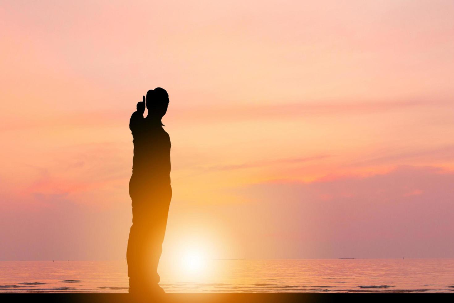 silueta de un hombre de negocios que da el pulgar hacia arriba como señal de un negocio exitoso en el fondo del cielo de la puesta de sol en la playa. foto