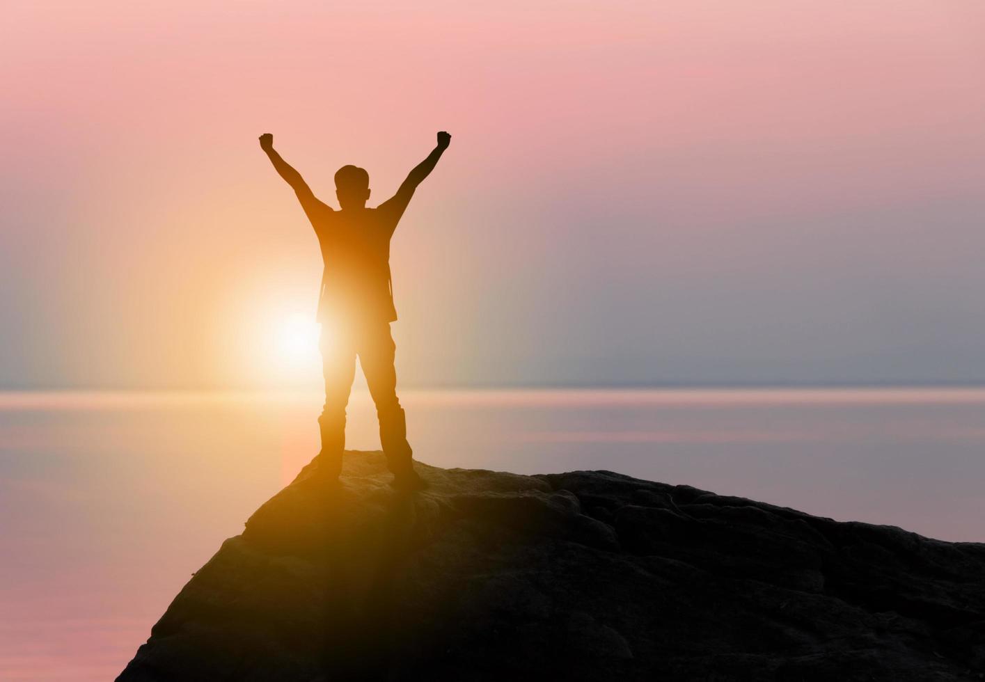 silueta de hombre de pie disfrutando en un cielo de atardecer tropical de piedra en el fondo de la playa, felicidad y concepto de vida activa. foto