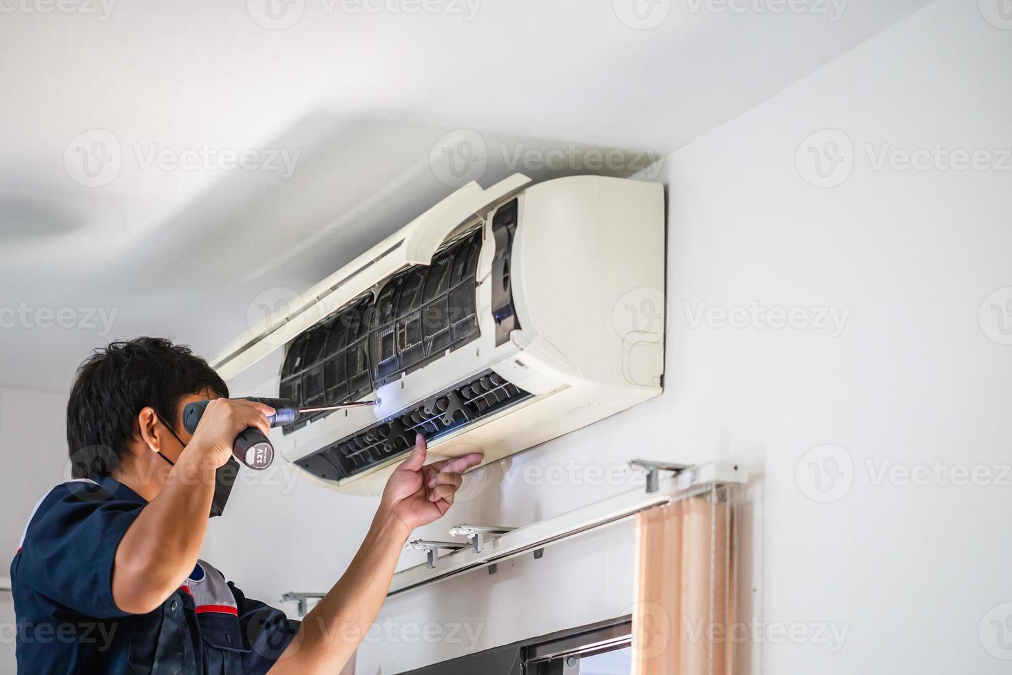 Male technician using a screwdriver fixing modern air conditioner, Male technician cleaning air conditioner indoors, Maintenance and repairing concepts photo