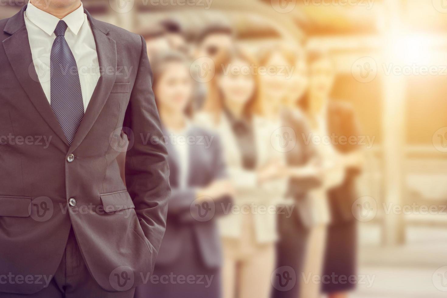 Close up of businessman standing with hands in pocket over blurry success business people team background photo