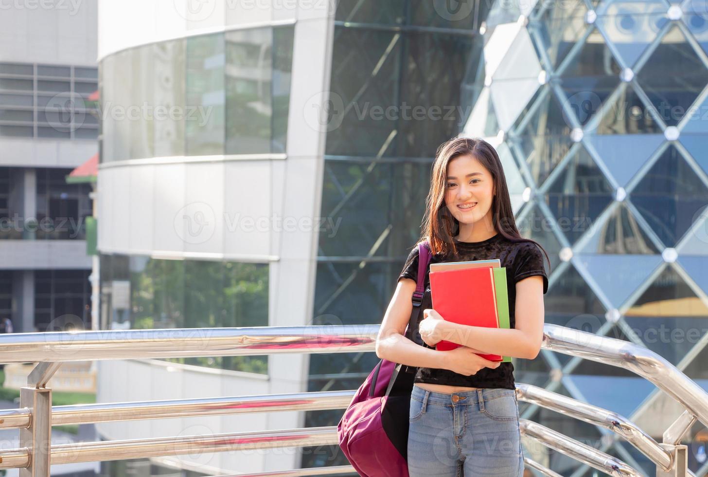 Portrait of a smiling female teenager with backpack and holding books photo