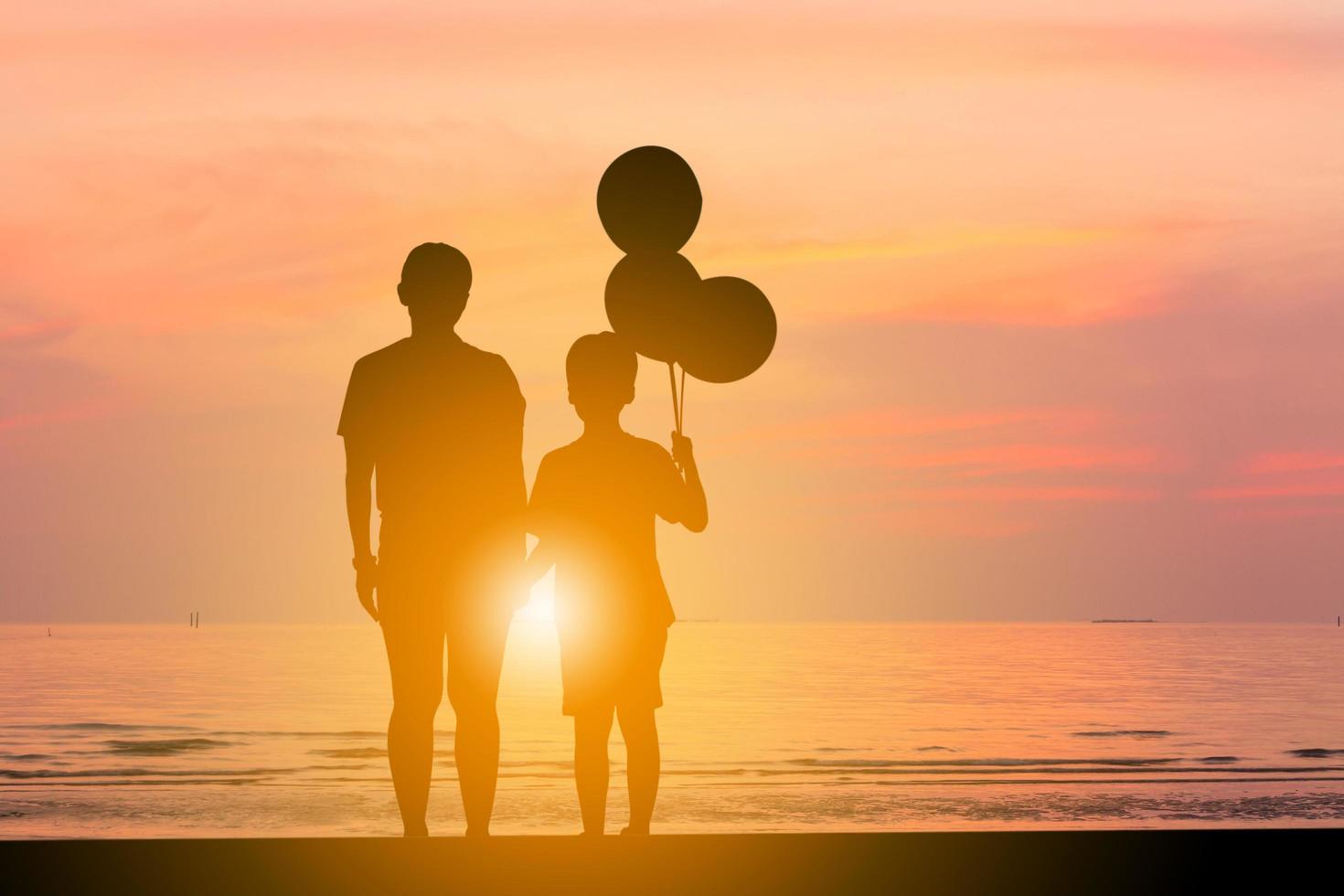 Silhouette of mother and son standing watching sunset on the beach with balloon in hand. photo