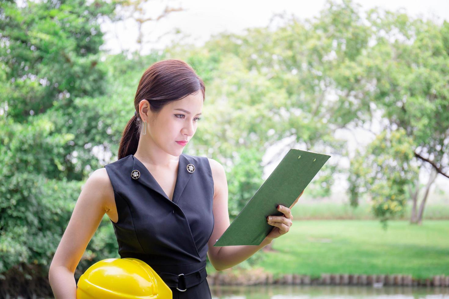 Young woman holding hardhat and looking at clipboard checklist, Quality control concept photo