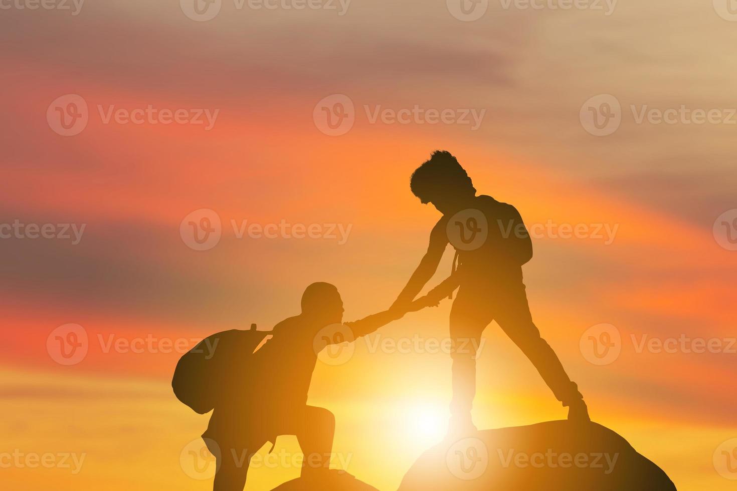 Silhouette of climbers man gived hand for pull hikers team to peak of mountain for work together, Sport and Teamwork Concept photo