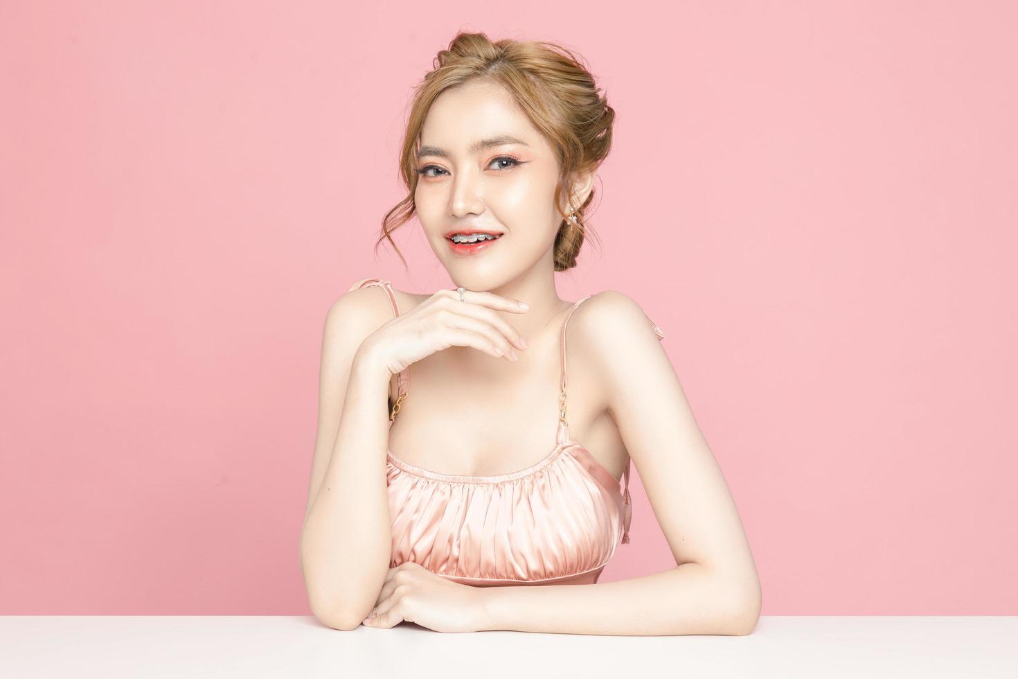 Beautiful young Asian woman have glitter on face wearing braces is feeling happy with clean fresh skin on pink background. Plastic surgery, Anti ageing, Cosmetology, beauty and spa, Female portrait. photo