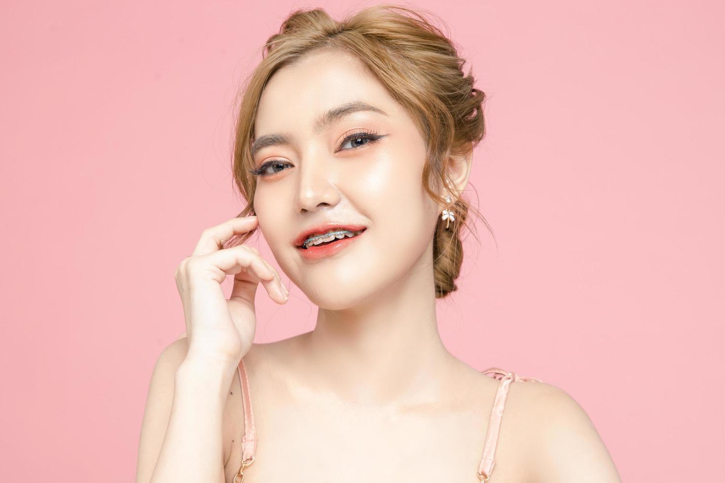 Beautiful young Asian woman have glitter on face wearing braces is feeling happy with clean fresh skin on pink background. Plastic surgery, Anti ageing, Cosmetology, beauty and spa, Female portrait. photo