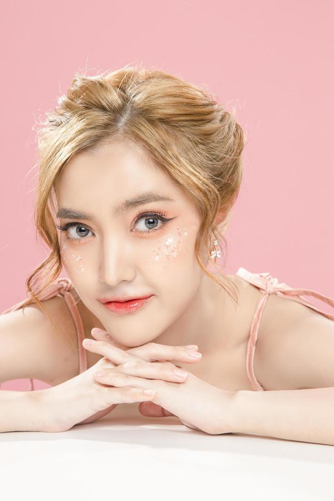 Beautiful young Asian woman have glitter on face wearing braces is feeling happy with clean fresh skin on pink background. Plastic surgery, Anti ageing, Cosmetology, beauty and spa, Female portrait. photo