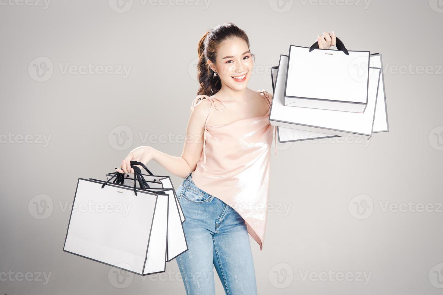 Beautiful young Asian woman is happy with many shopping bags in her hand isolated on grey banner background. photo