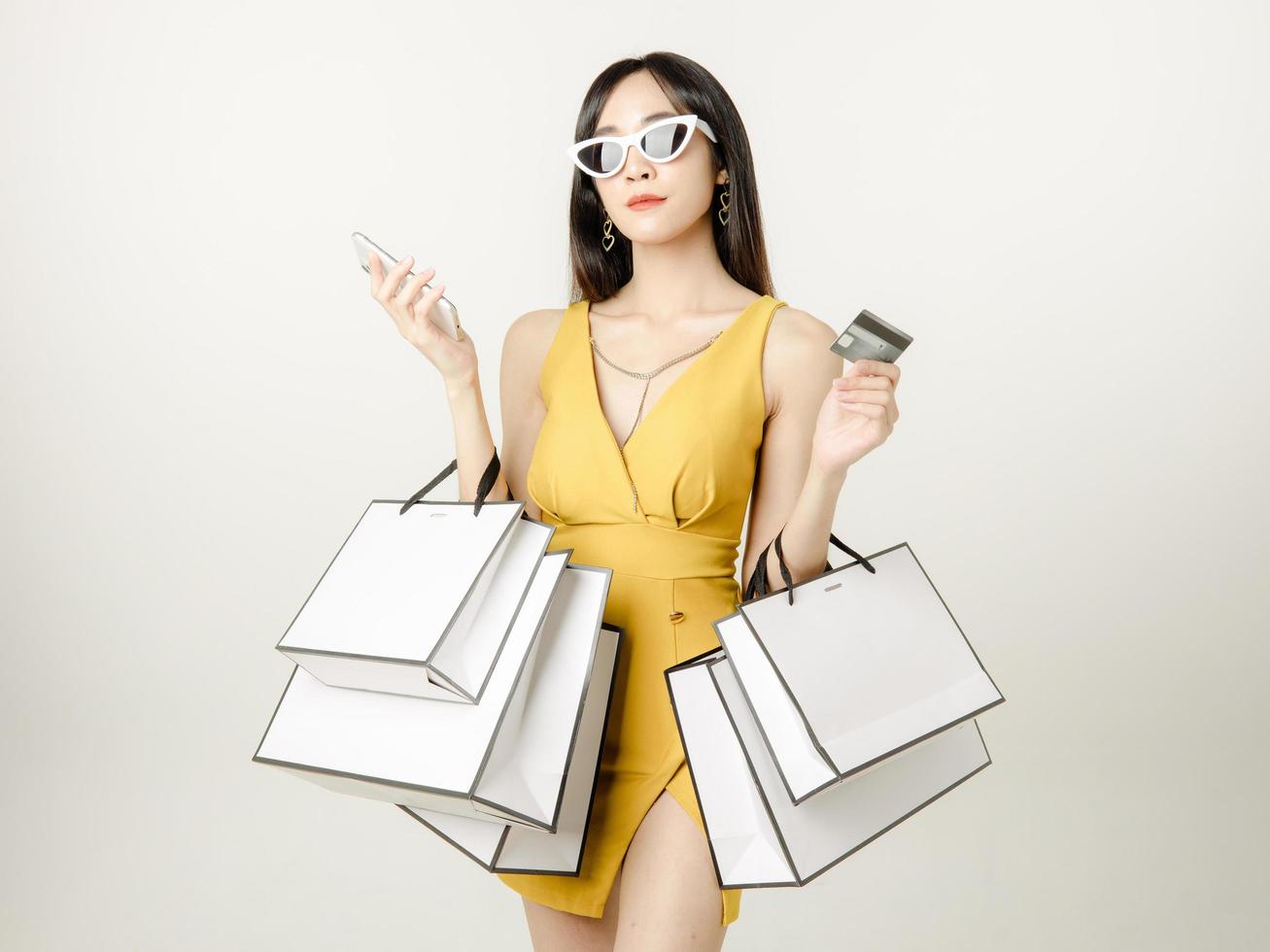 una mujer asiática segura de sí misma con un vestido amarillo sensual que usa gafas de sol y lleva una bolsa de compras se está divirtiendo comprando. foto