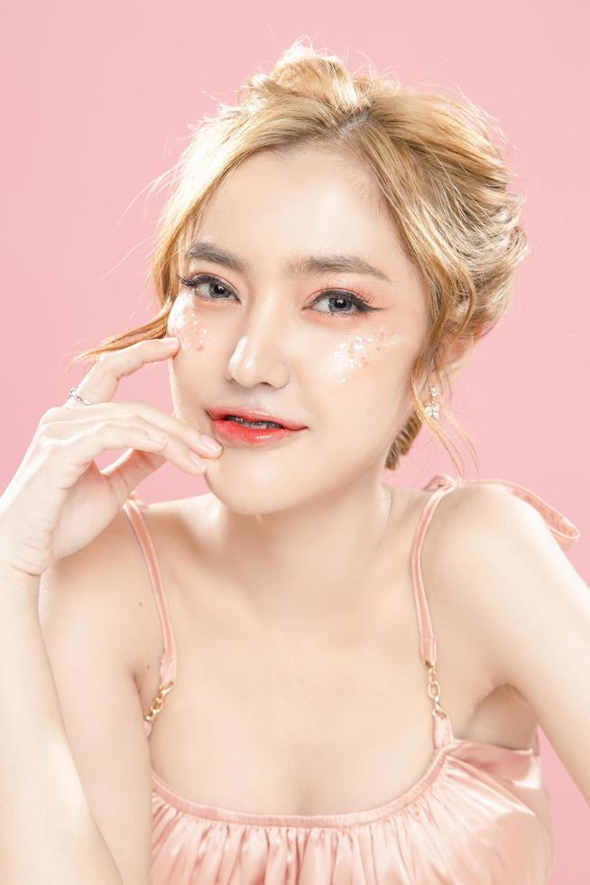 Beautiful young Asian woman have glitter on face wearing braces is feeling happy with clean fresh skin on pink background. Plastic surgery, Anti ageing, Cosmetology, beauty and spa, Female portrait. photo