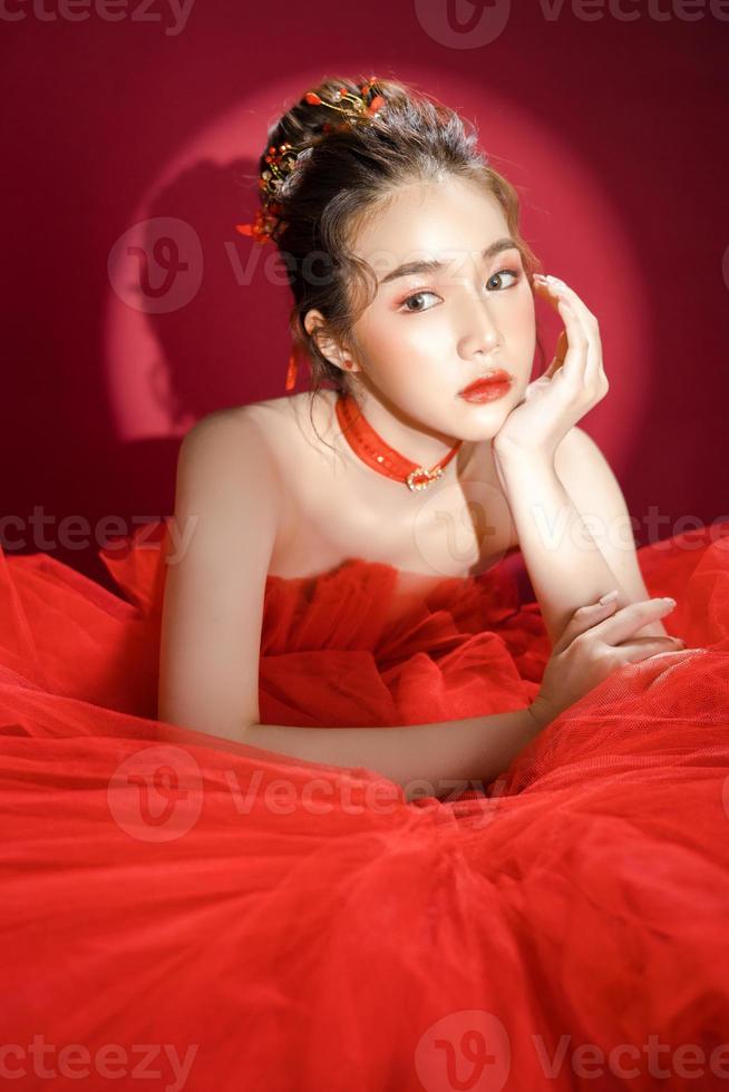 joven modelo asiático de mujer bonita con un elegante vestido rojo de lujo con un fondo rojo aislado. foto