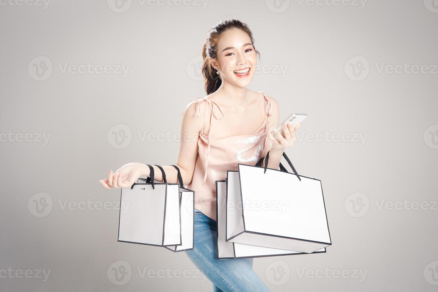 Beautiful young Asian woman is happy with many shopping bags in her hand isolated on grey banner background. photo