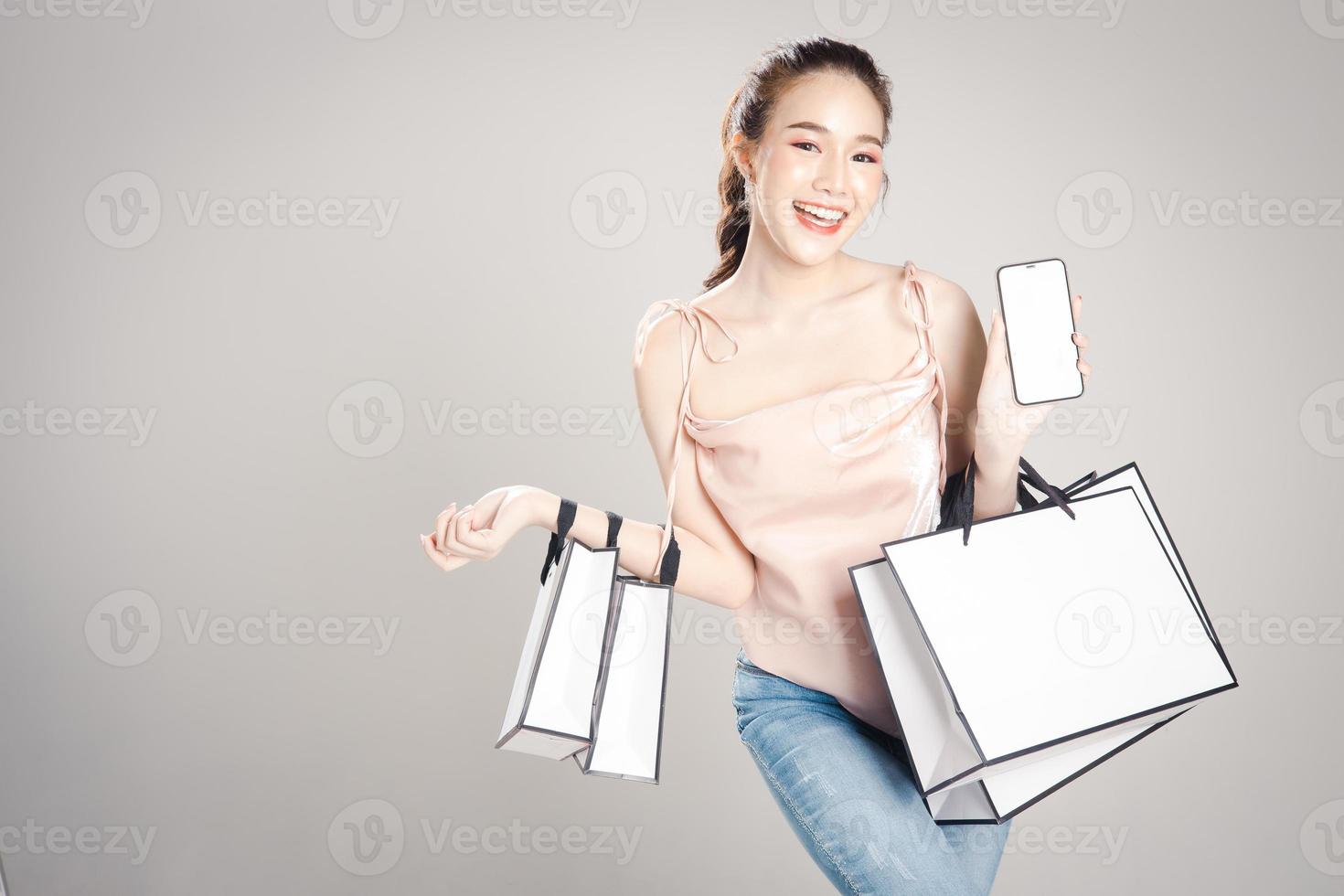 Beautiful young Asian woman is happy with many shopping bags in her hand isolated on grey banner background. photo