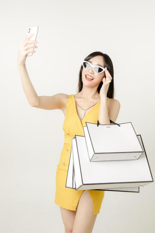 Confident Asian woman in a sultry yellow dress wearing sunglasses and carrying a shopping bag is having fun shopping. photo