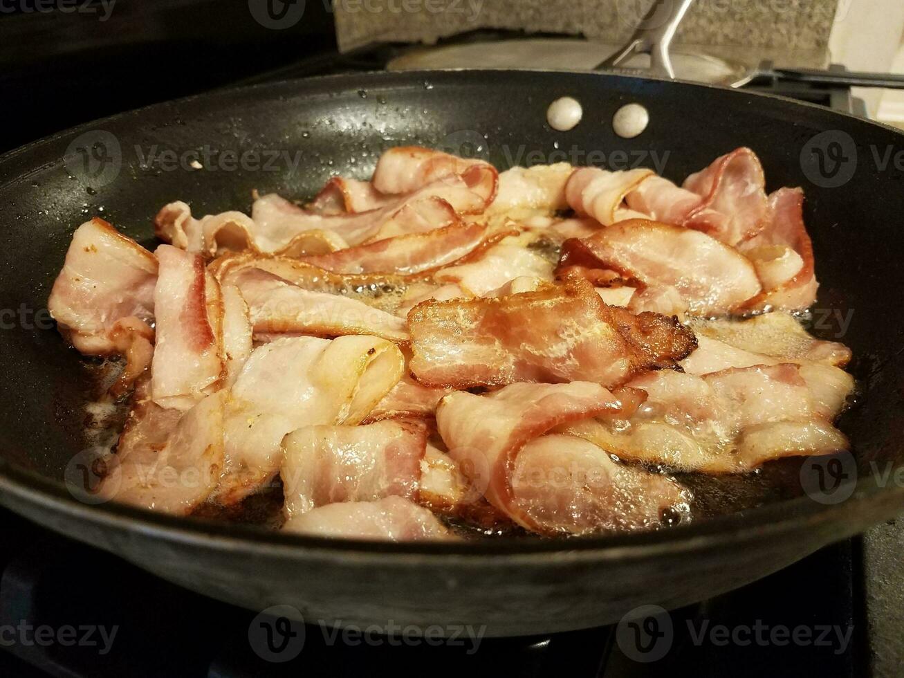 bacon cooking in frying pan or skillet on stove photo