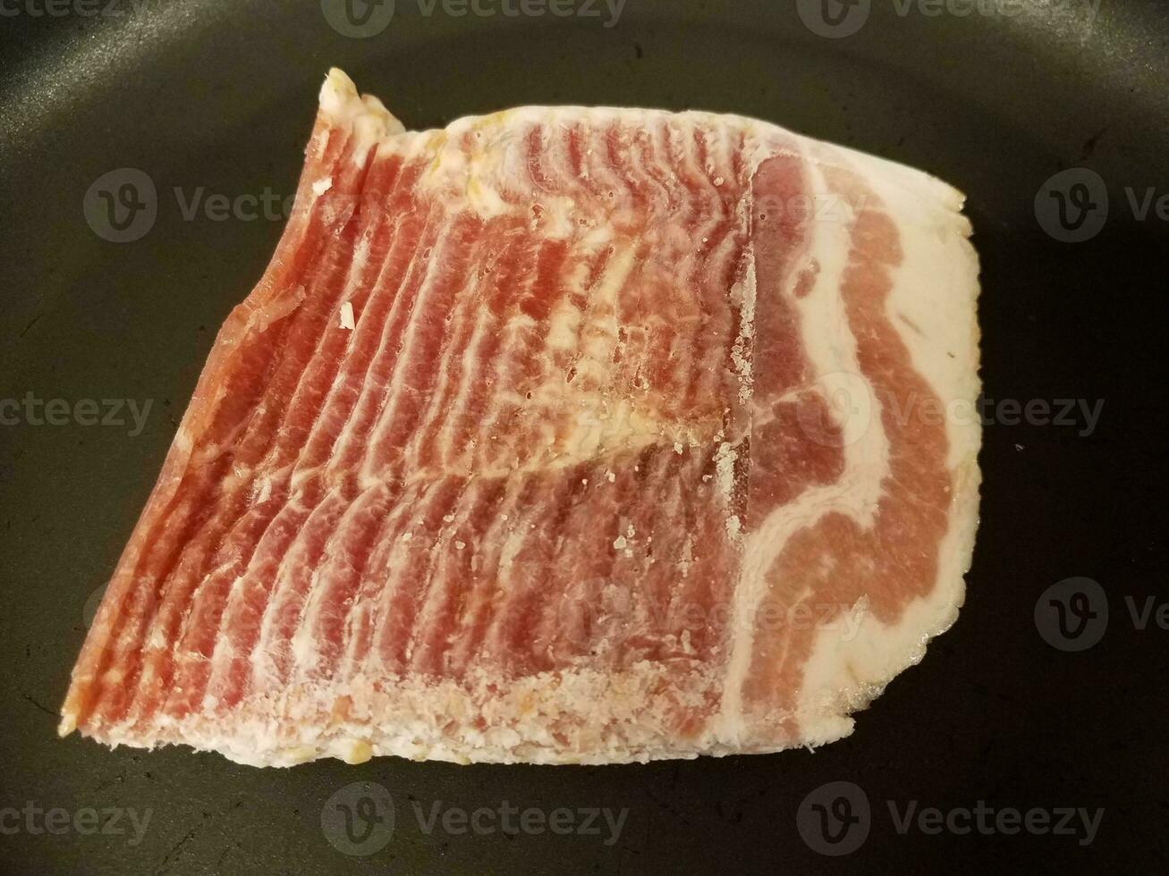 raw frozen bacon strips in frying pan or skillet photo