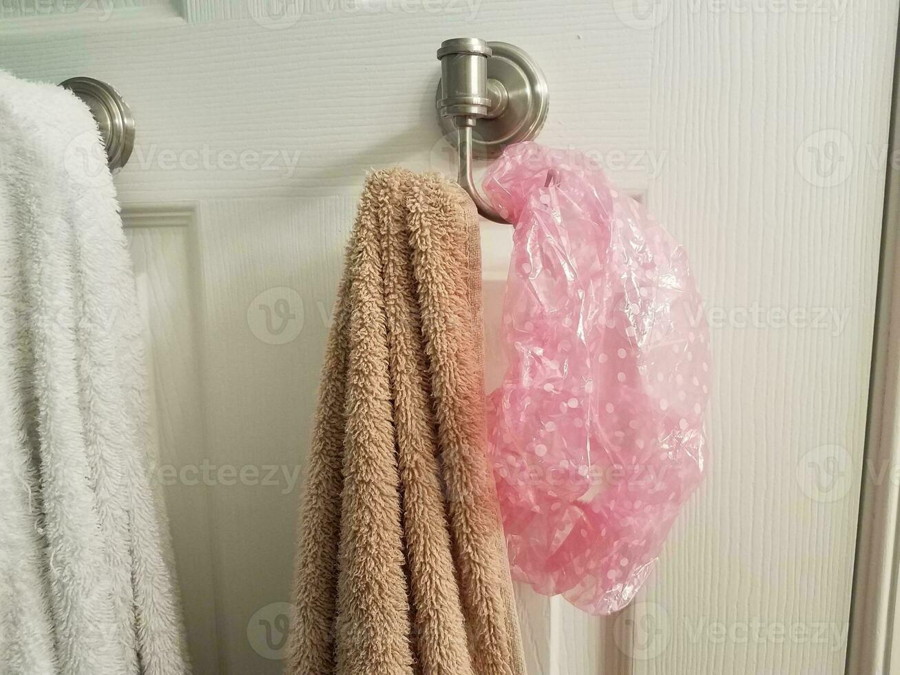 white and brown towel on hook on bathroom door with pink showercap photo