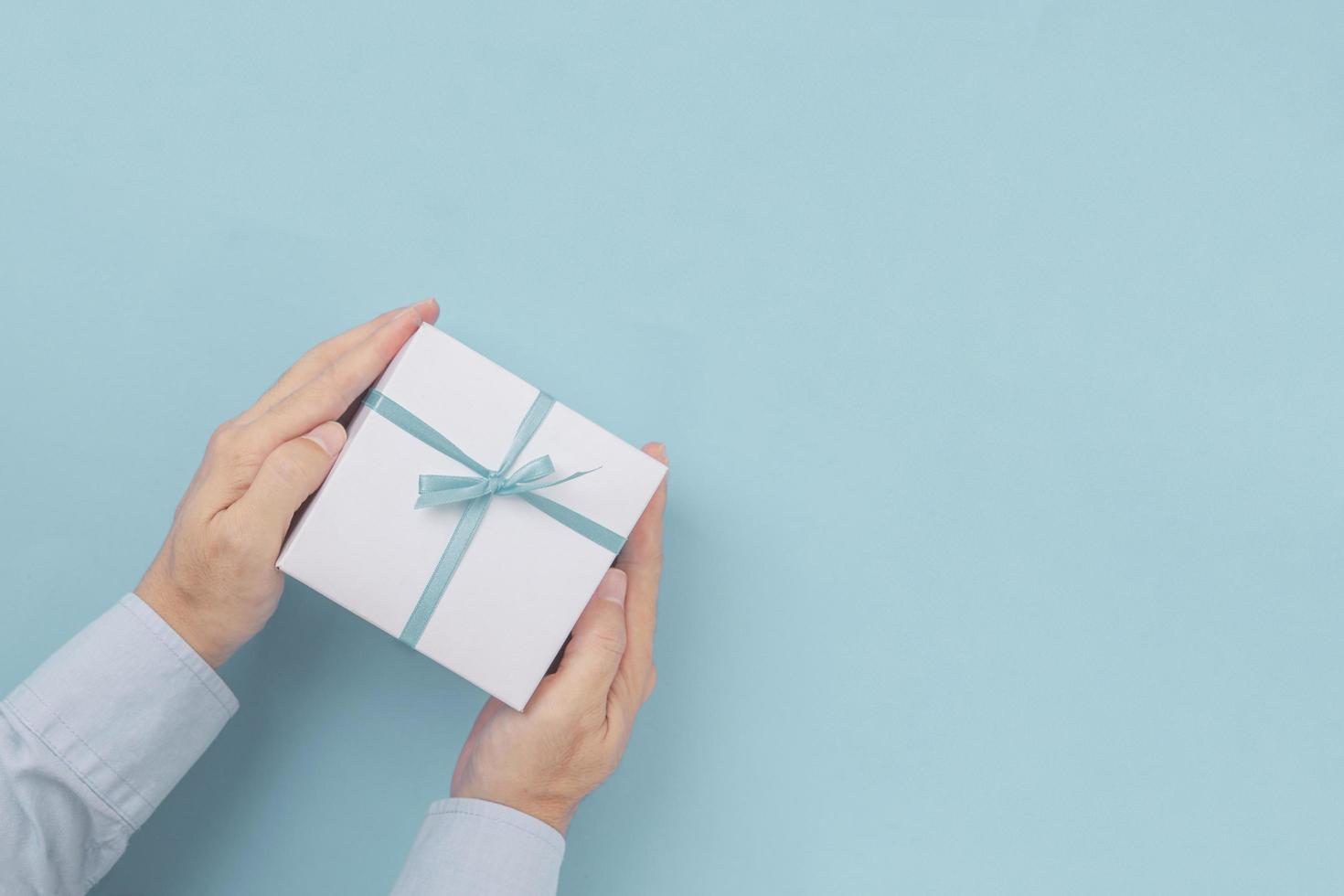 Hands holding Gift box with blue bow with copy space in craft paper over blue background. Top view, flat lay photo