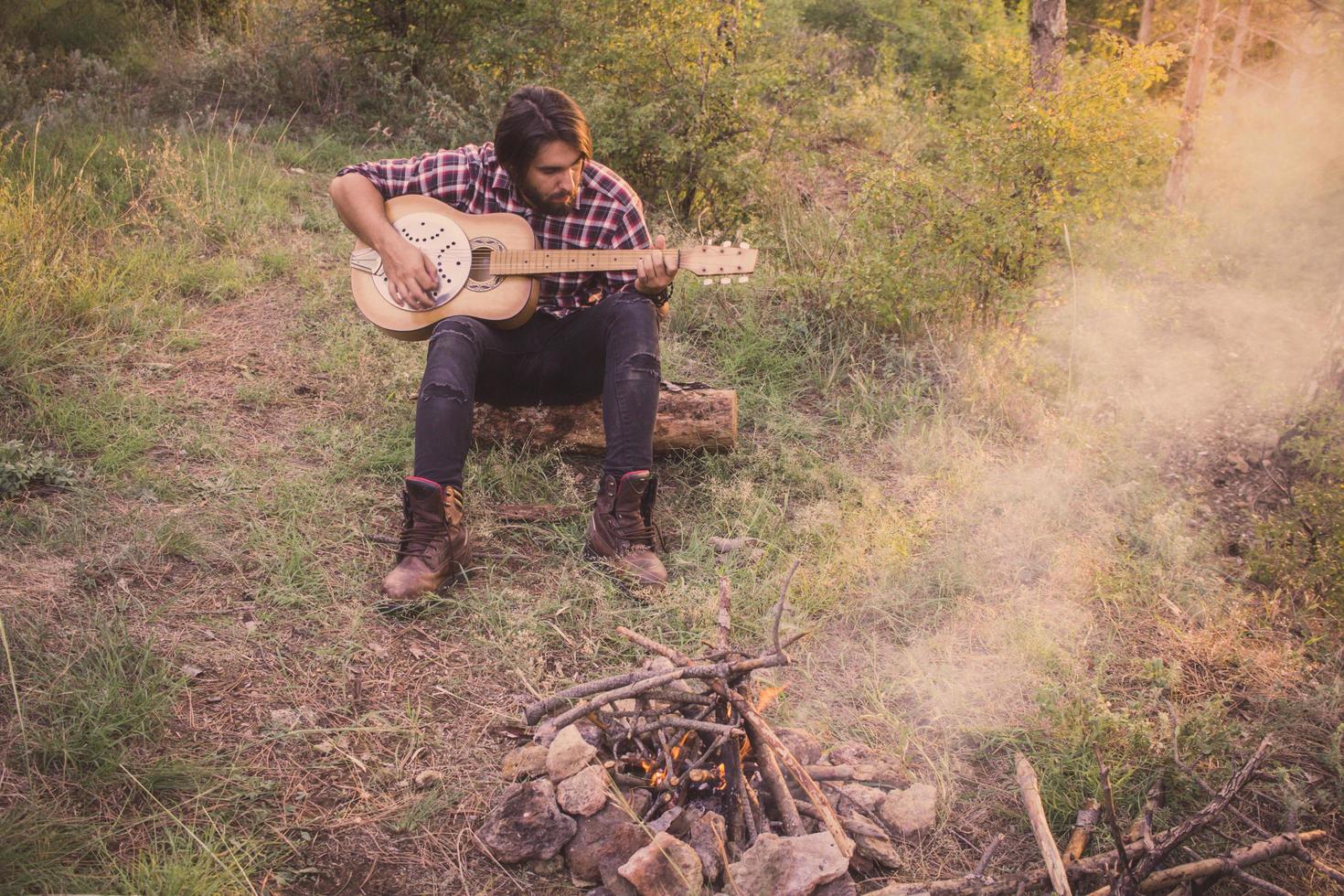 Folk or country guitar player in the forest with dog, man in woods, campfire and sunset background photo