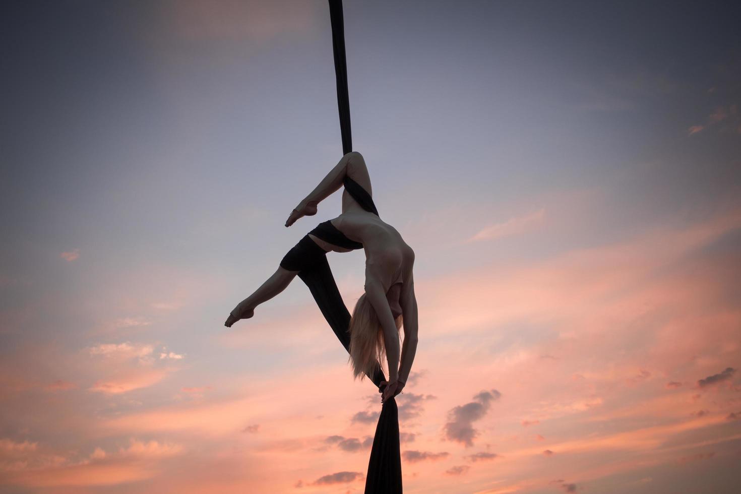 exercises with aerial silk outdoor, sky background. beautiful fit woman training acrobatic in airt. photo