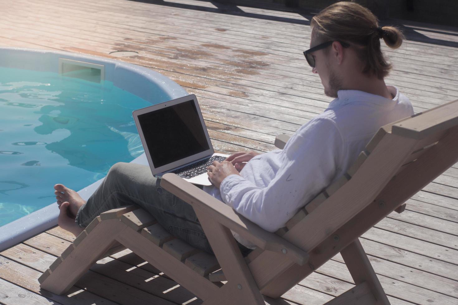 young men with laptopp working near the pool, freelancer in hotel on vacation with notebook photo