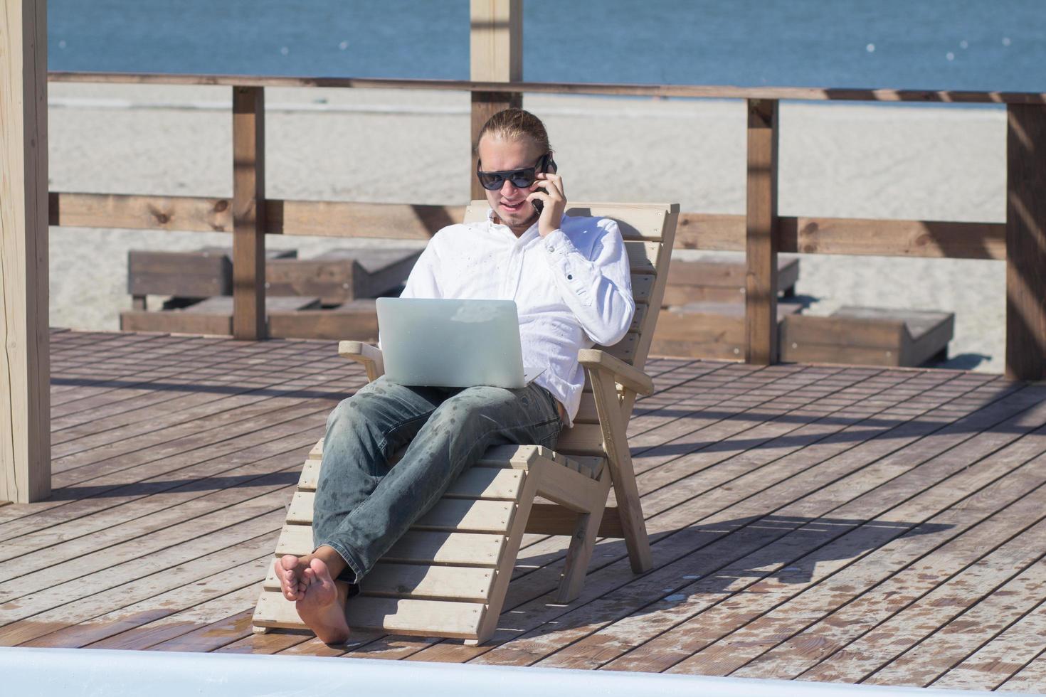 young men with laptopp working near the pool, freelancer in hotel on vacation with notebook photo
