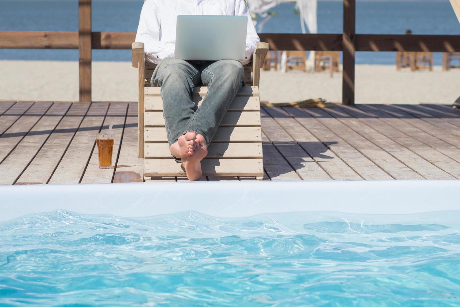 young men with laptopp working near the pool, freelancer in hotel on vacation with notebook photo