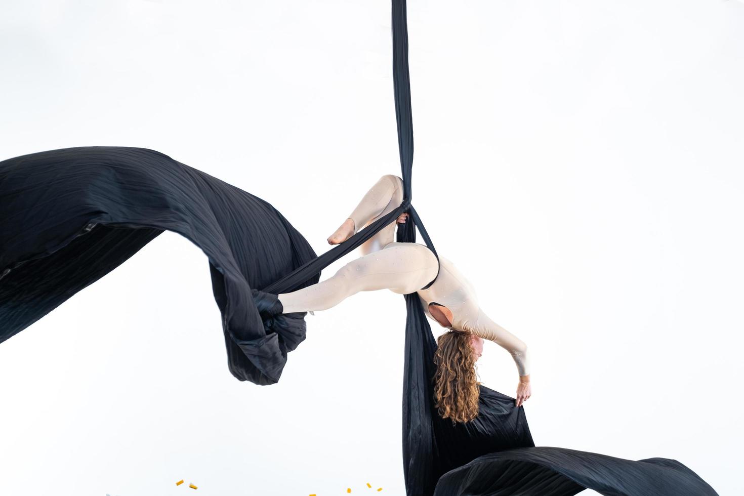 Woman hanging in aerial silk in white studio photo