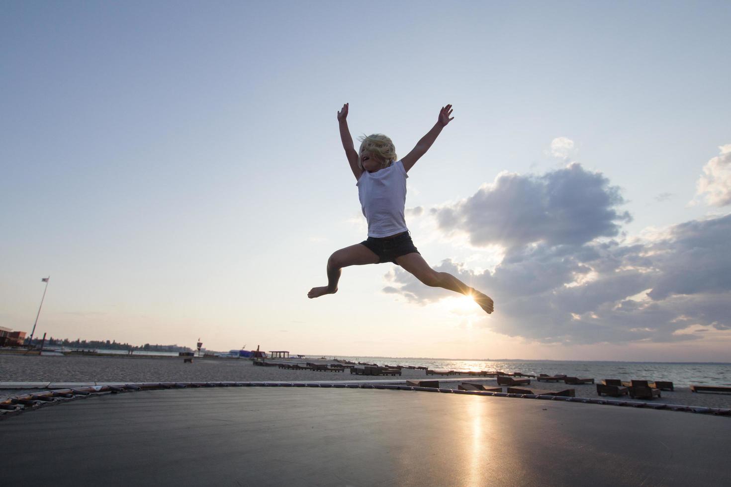 niña salta y se divierte en el trampolín en verano foto