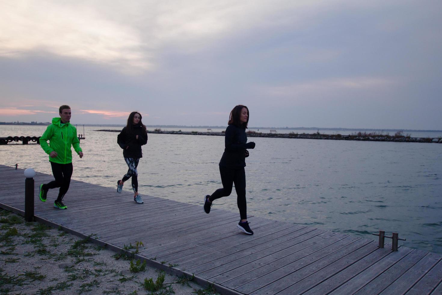 group of young people training outdoors, runners exercises, sea or river background photo
