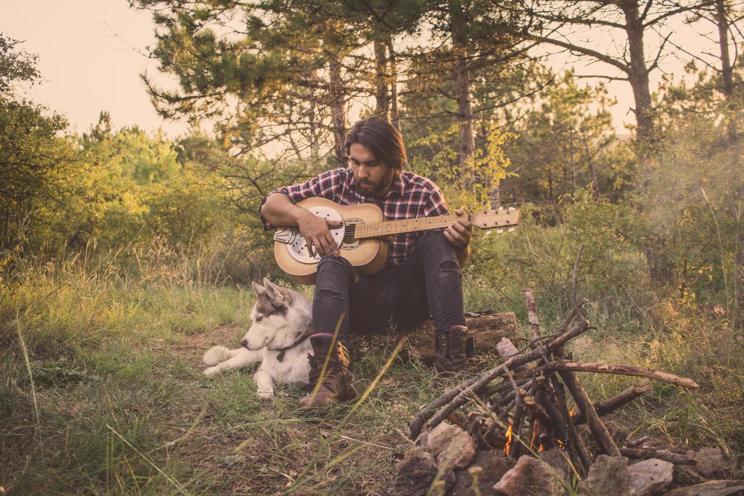 Folk or country guitar player in the forest with dog, man in woods, campfire and sunset background photo