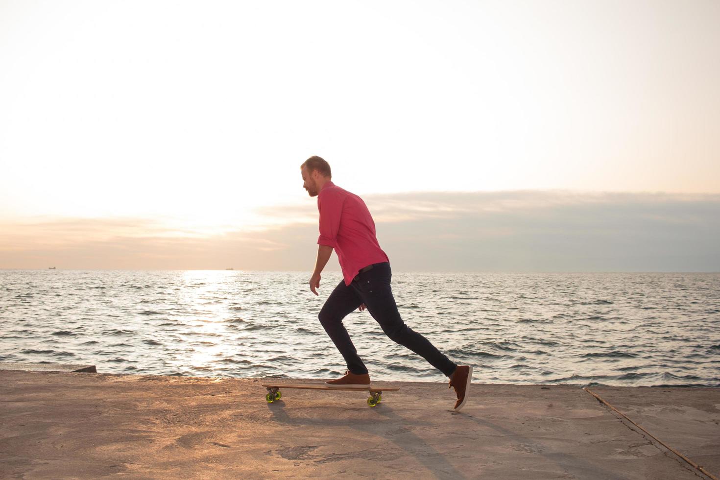skater with backpack watching sunrise or sunset in the sea or ocean photo