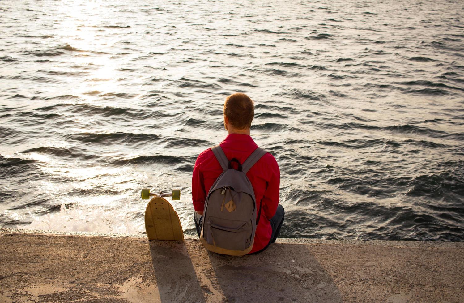 patinador con mochila viendo el amanecer o el atardecer en el mar o el océano foto