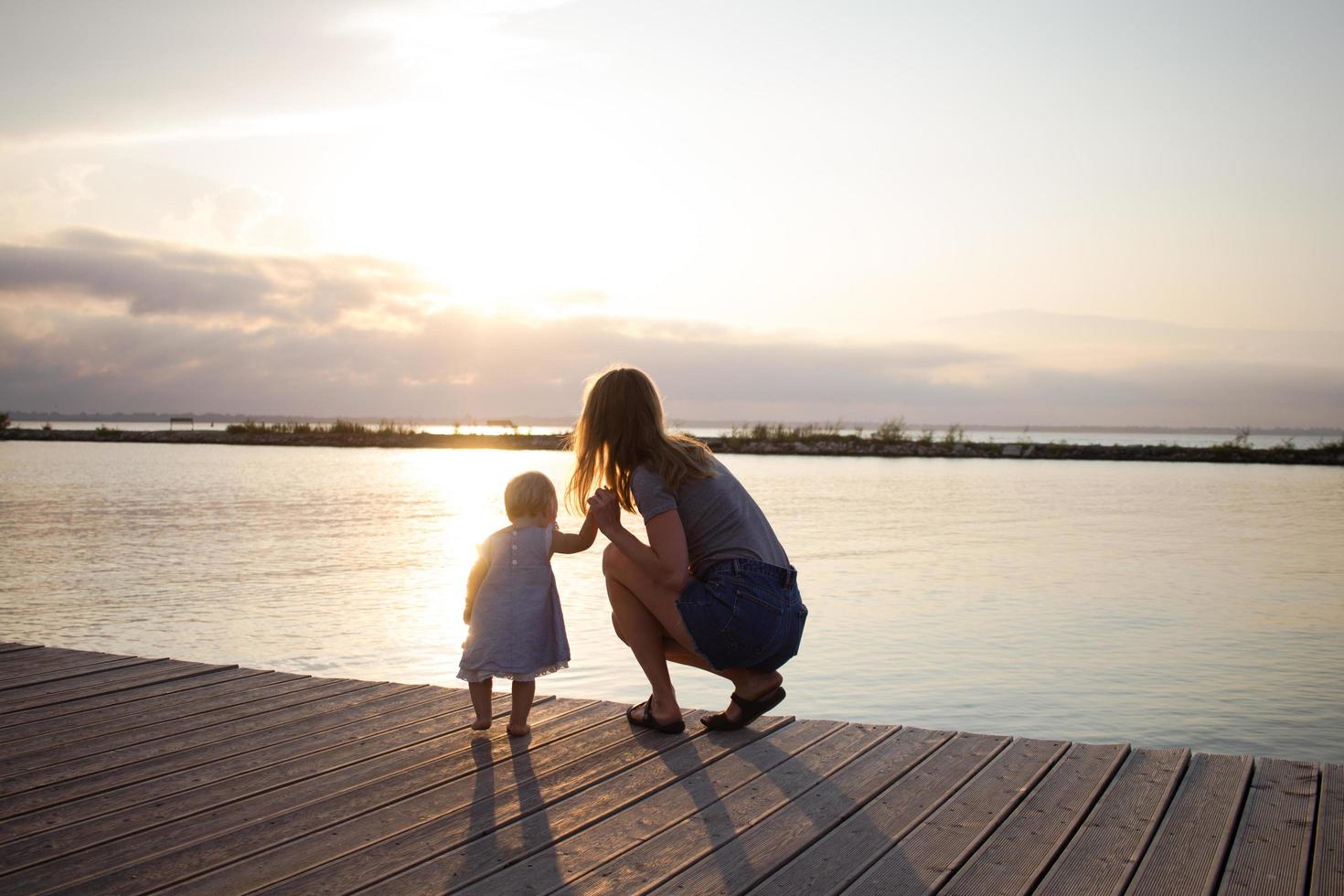 madre e hija caminando en el muelle de madera en un día soleado, familia feliz en la playa foto