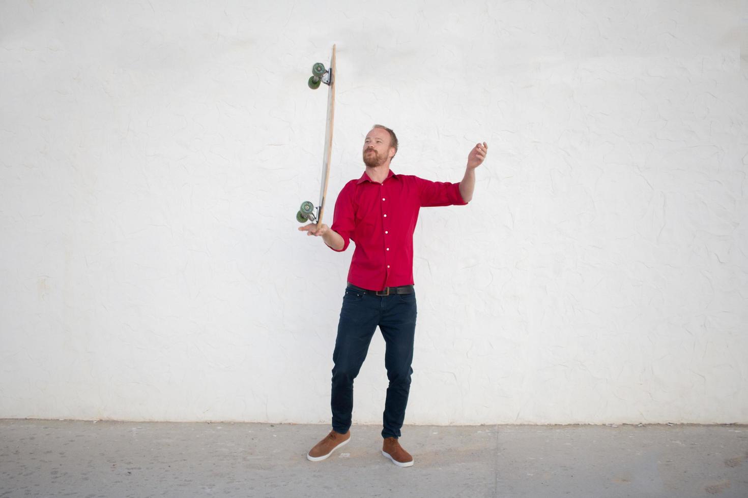 Young bearded man riding on skateboard, hipster with longboard in red shirt and blue jeans urban background photo