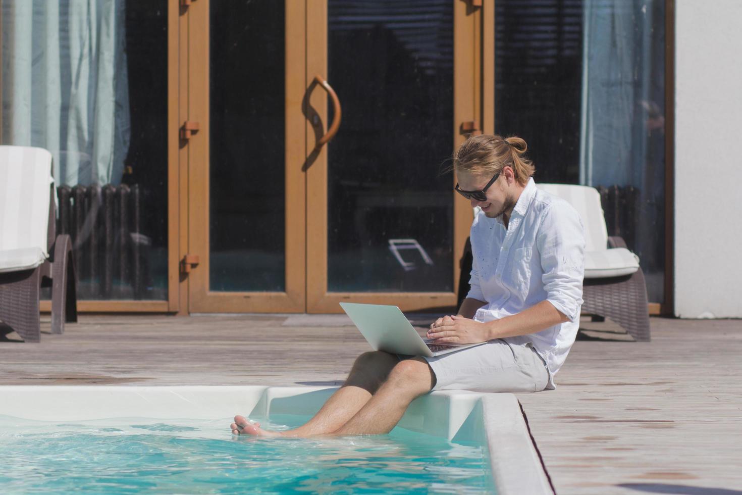 young men with laptopp working near the pool, freelancer in hotel on vacation with notebook photo