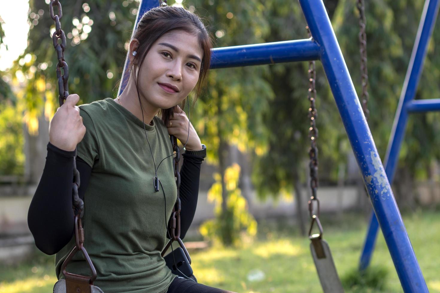 Teenage girl sitting on a swing chain smiling. photo