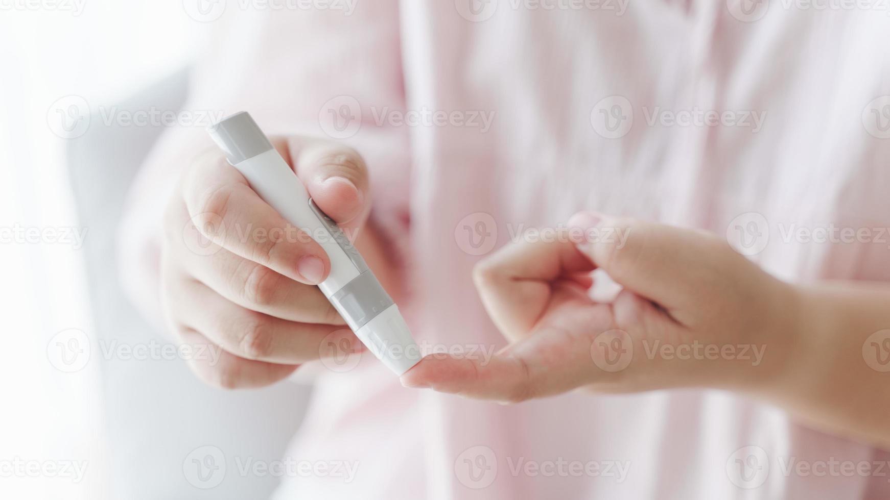 Asian woman using lancet on finger for checking blood sugar level by Glucose meter, Healthcare and Medical, diabetes, glycemia concept photo