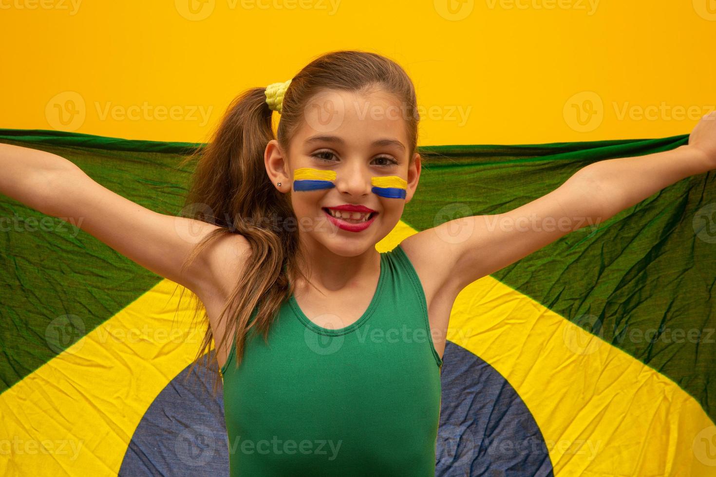 Football supporter, Brazil team. World Cup. Beautiful little girl cheering for her team on yellow background photo