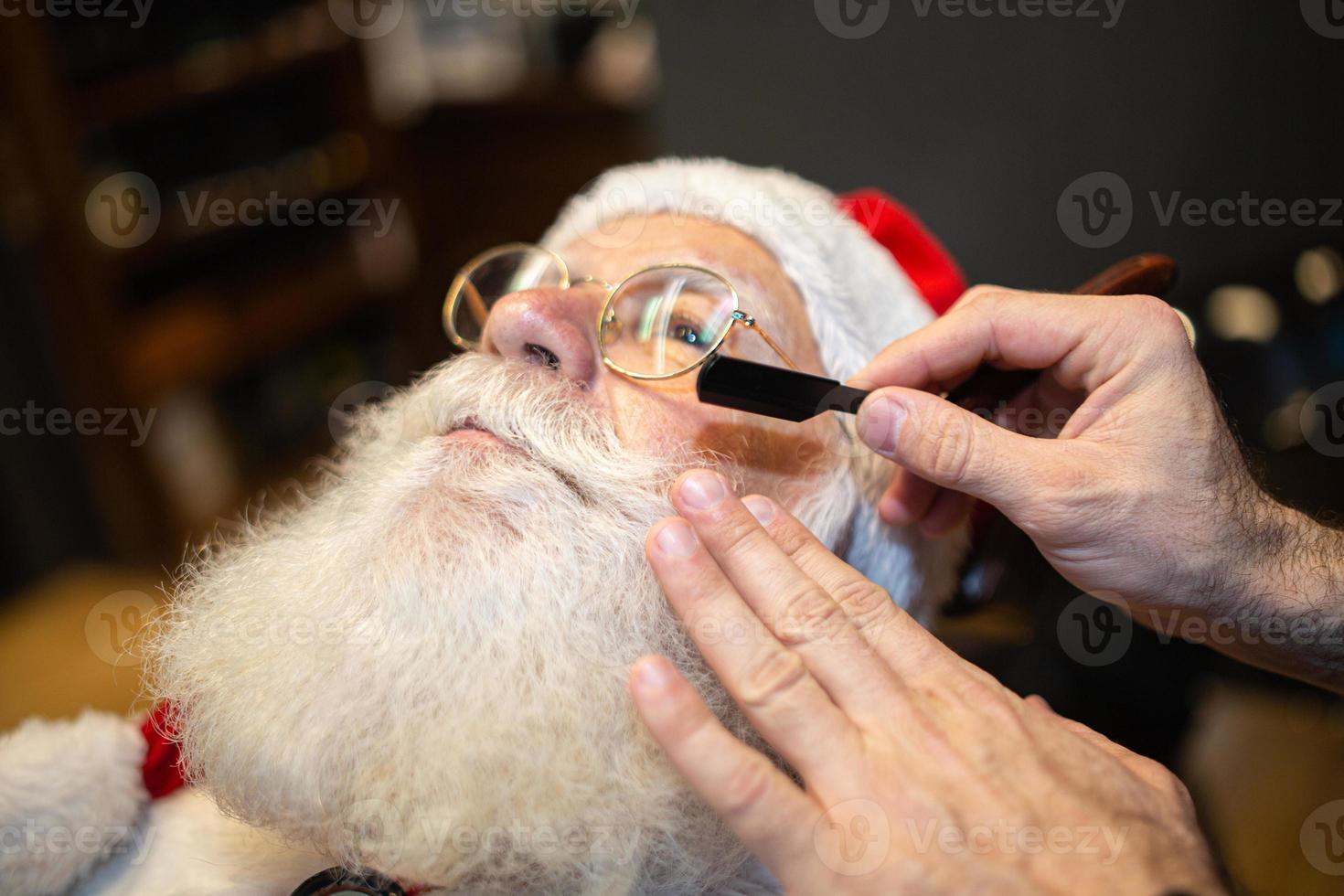 Santa Claus shaving in barbershop. Looking in the mirror. Getting ready for Christmas. Beautifying for the holidays. Bearded. Cuting. photo