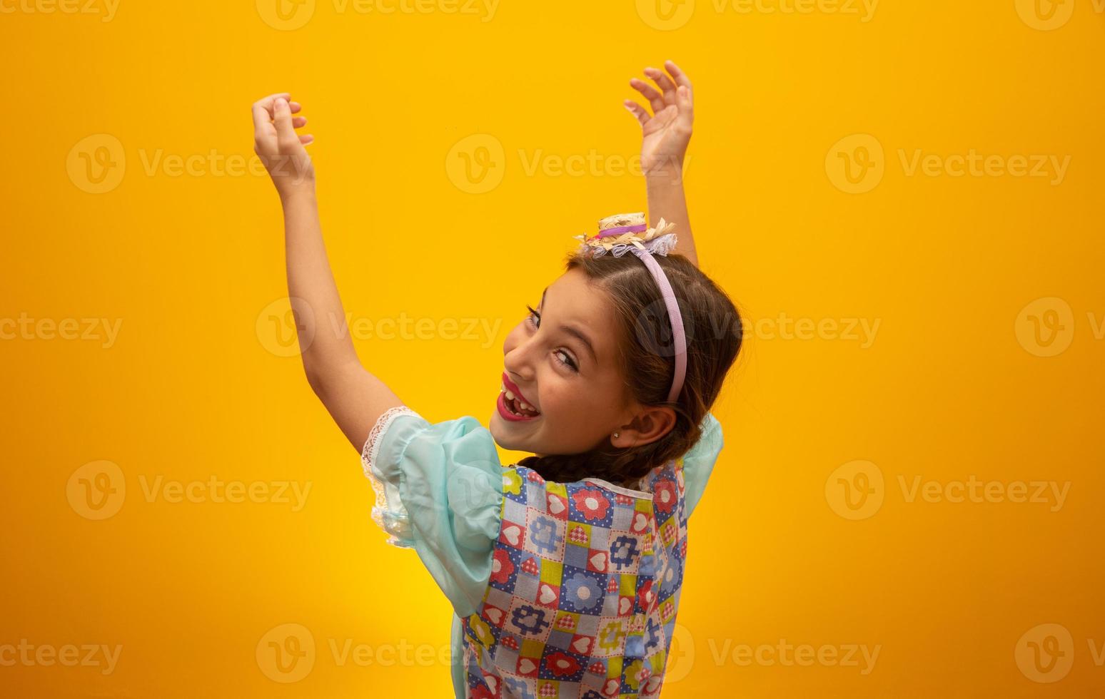 Child in typical clothes of famous Brazilian party called Festa Junina in celebration of Sao Joao. Beautiful girl on yellow background. photo