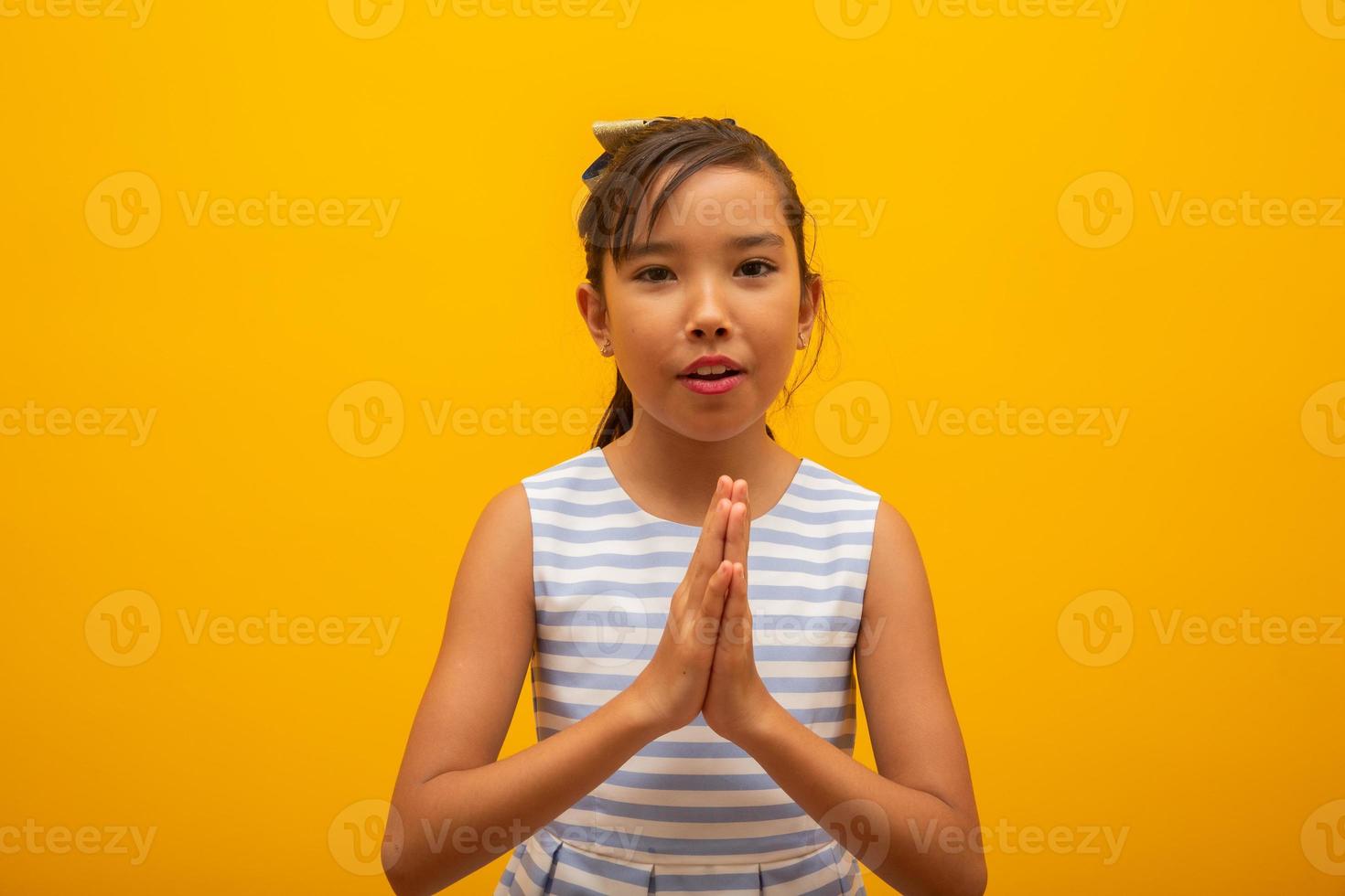 Little girl praying on yellow background. Little asian girl hand praying, hands folded in prayer concept for faith, spirituality and religion. photo