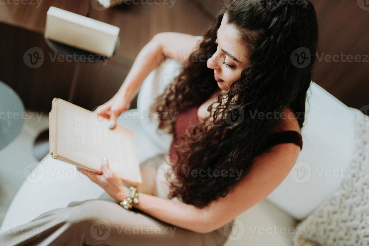 A Latin girl reading a book on the sofa at home. photo