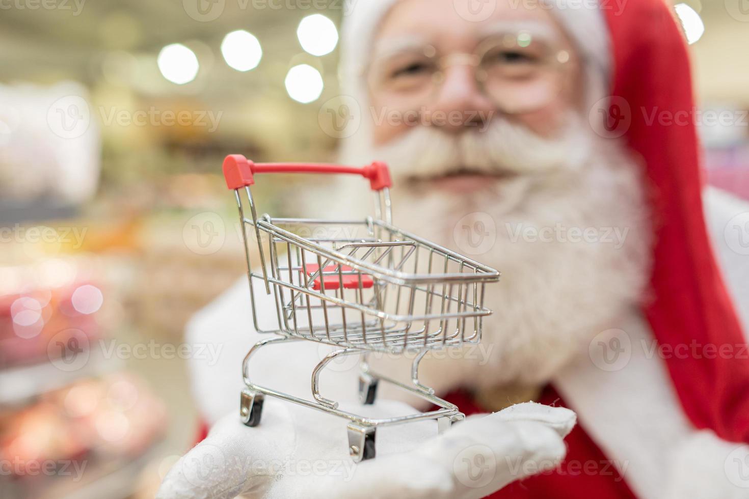 Santa Claus doing grocery shopping at the supermarket, he is showing a mini cart, Christmas and shopping concept. photo