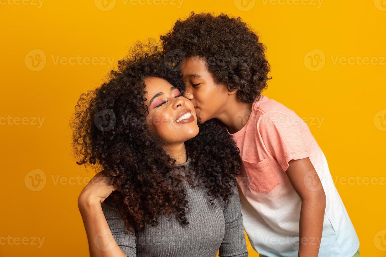 Portrait of young African American mother with toddler son. Son kissing his mother. Yellow background. Brazilian family. photo