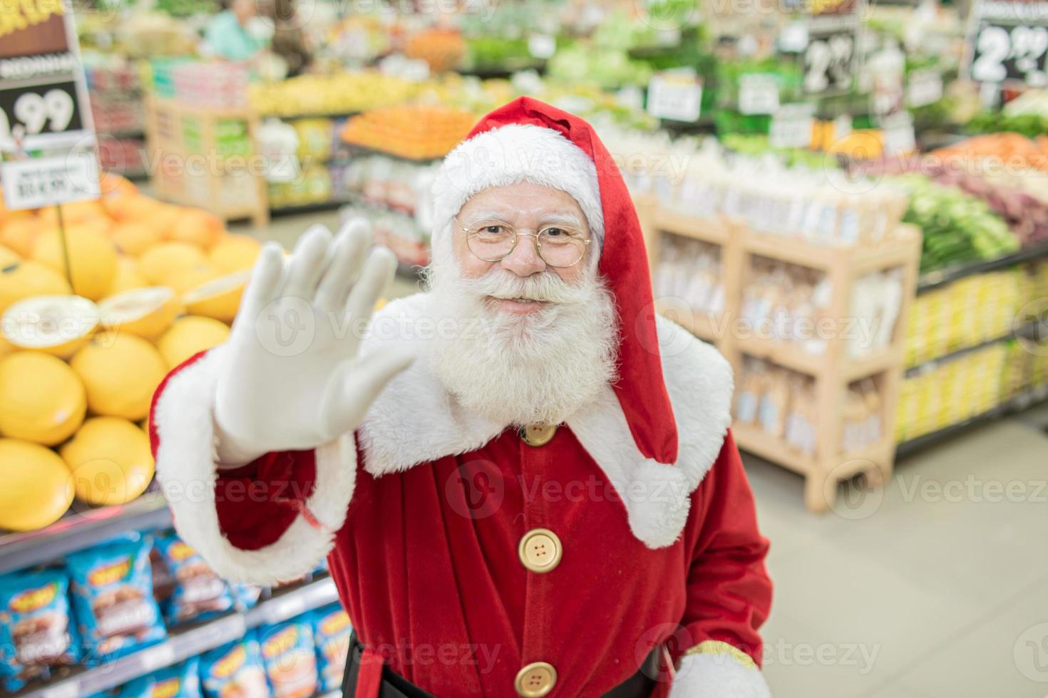 santa claus haciendo compras en el supermercado, está empujando un carrito lleno, navidad y concepto de compras. foto