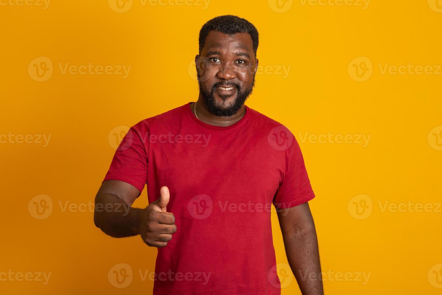 Positive dark skinned male has joyful expression and broad smile with white teeth, being in good mood, thumbs up, ok, okay isolated over yellow studio wall with copy space. Brazilian middle aged guy. photo