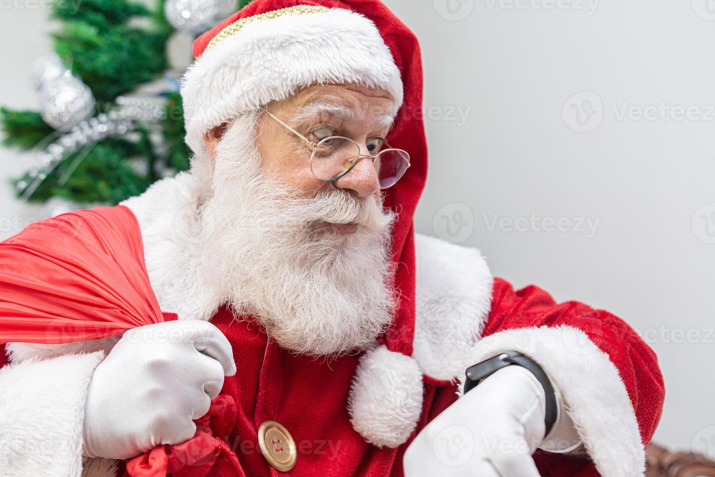 Santa Claus is late. He looks scared at the clock. Santa Claus wears a modern clock. Countdown. The time is coming. photo