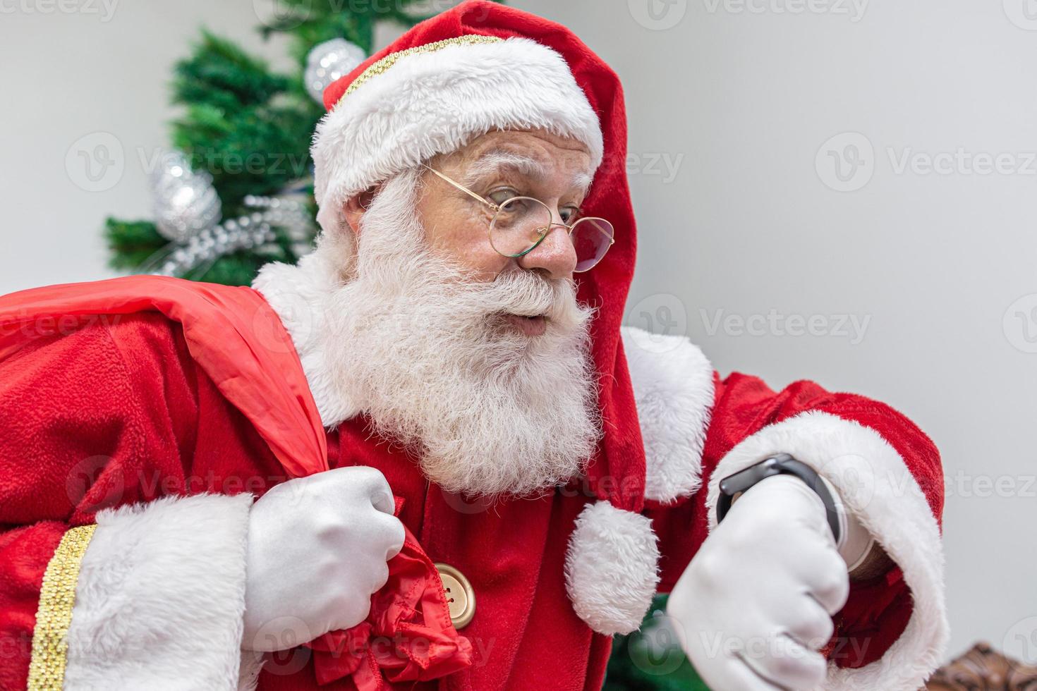 Santa Claus is late. He looks scared at the clock. Santa Claus wears a modern clock. Countdown. The time is coming. photo