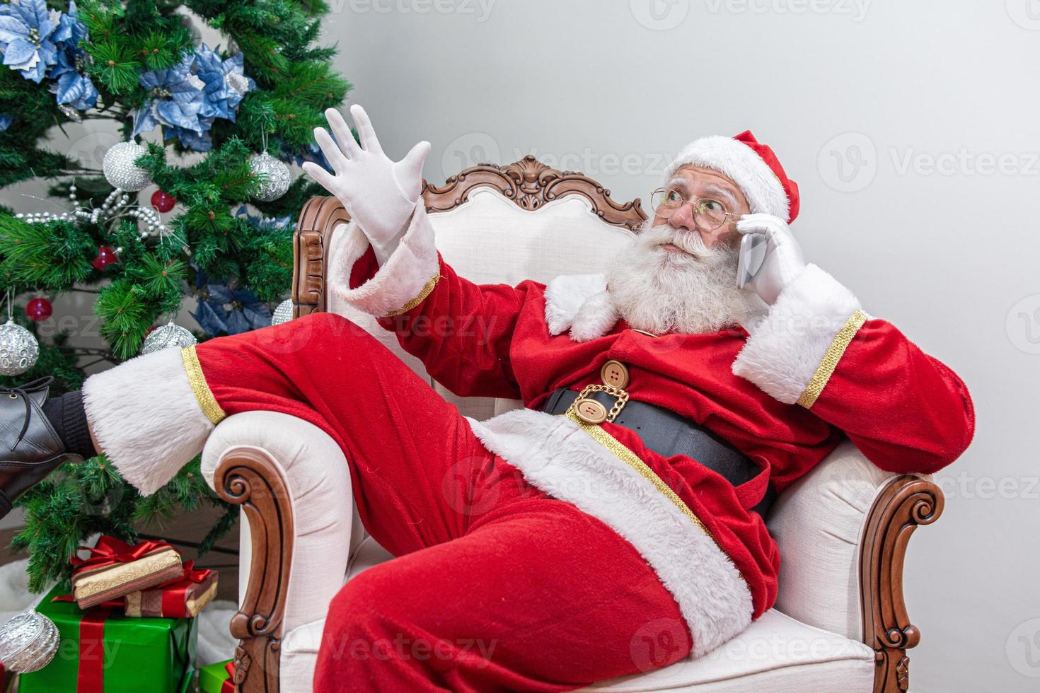 santa claus usando un teléfono inteligente. hablando por teléfono con un niño. analizando las solicitudes de navidad. foto